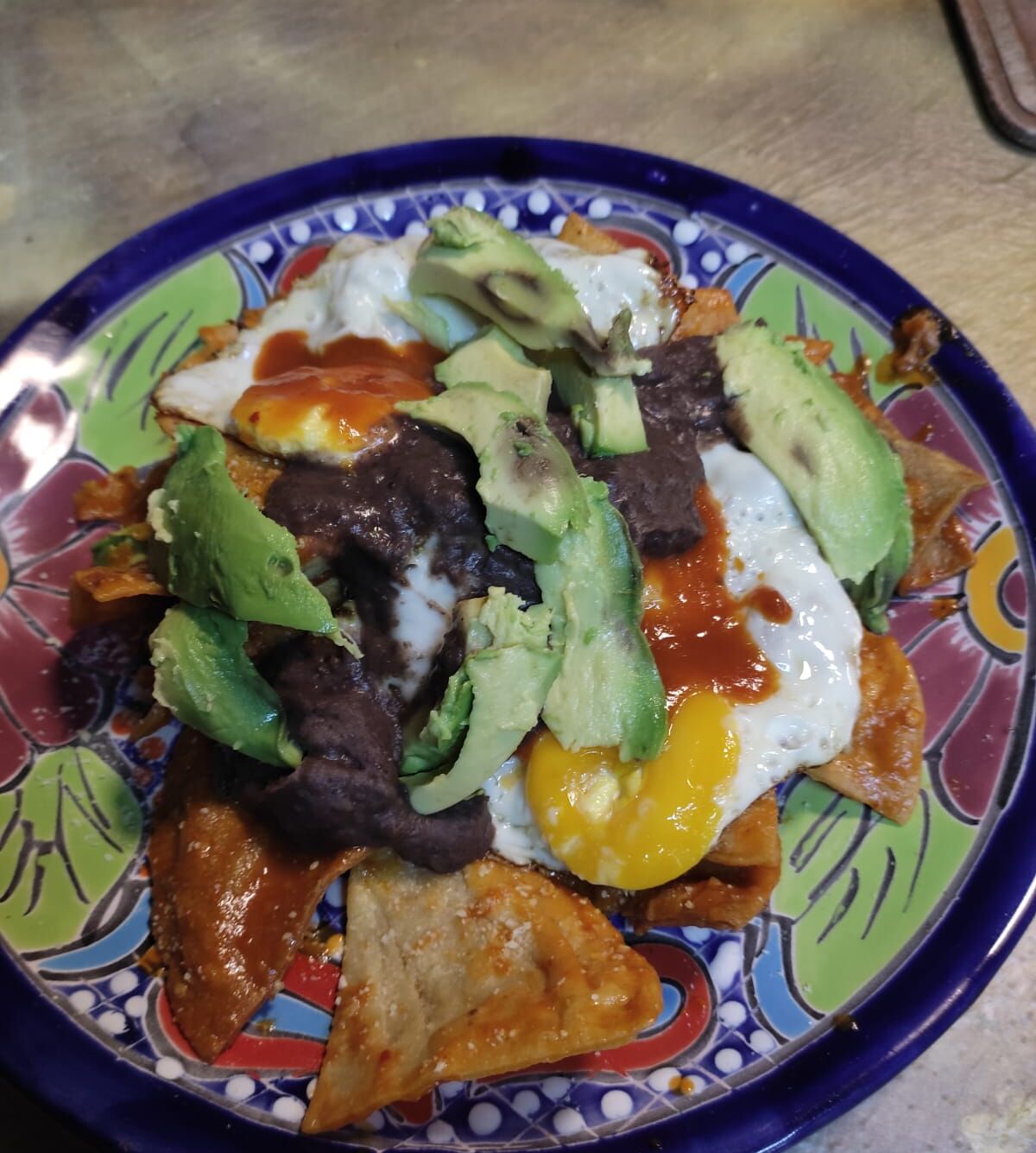 A plate of nachos with toppings including avocado, eggs, and a sauce.