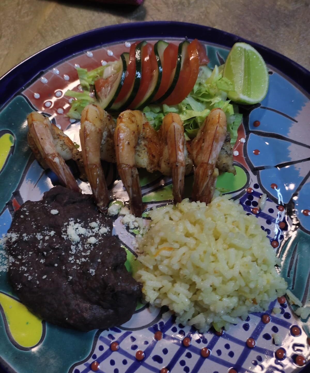A plate with grilled shrimp, rice, refried beans, and a slice of lime.
