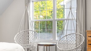 A room with a bed, two white macramé chairs, a small round table, and a window with a view of trees. - Stunning 5 Bed 2.5 Bath in the Heart of Clarksville (Clarksville)