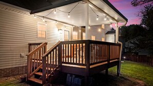 A covered deck with wooden railings and string lights, attached to a house with white siding. - Stunning 5 Bed 2.5 Bath in the Heart of Clarksville (Clarksville)