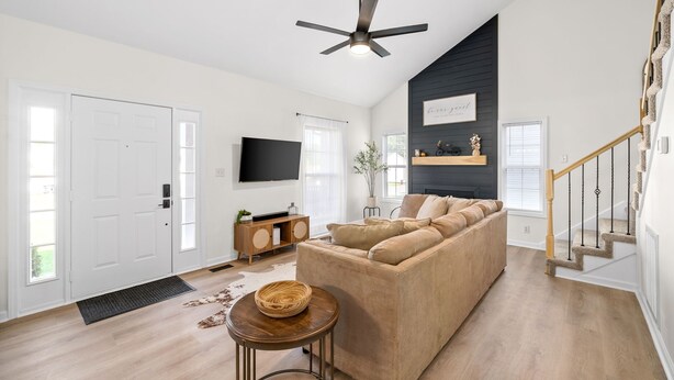 A modern living room with a beige sofa, a wooden side table, and a ceiling fan. - Stunning 5 Bed 2.5 Bath in the Heart of Clarksville (Clarksville)