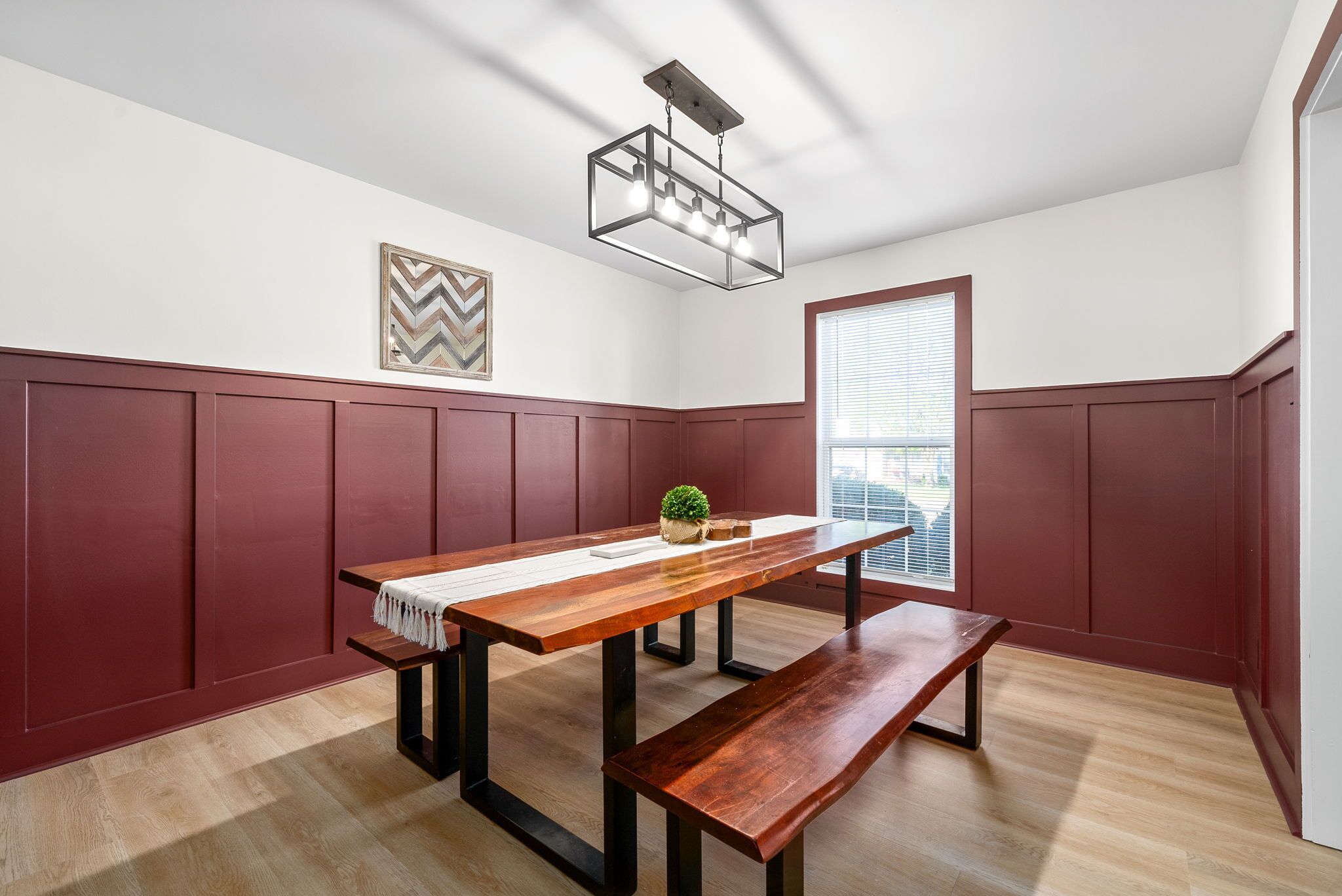 A dining area with a wooden table, bench, pendant light, and a window with blinds.