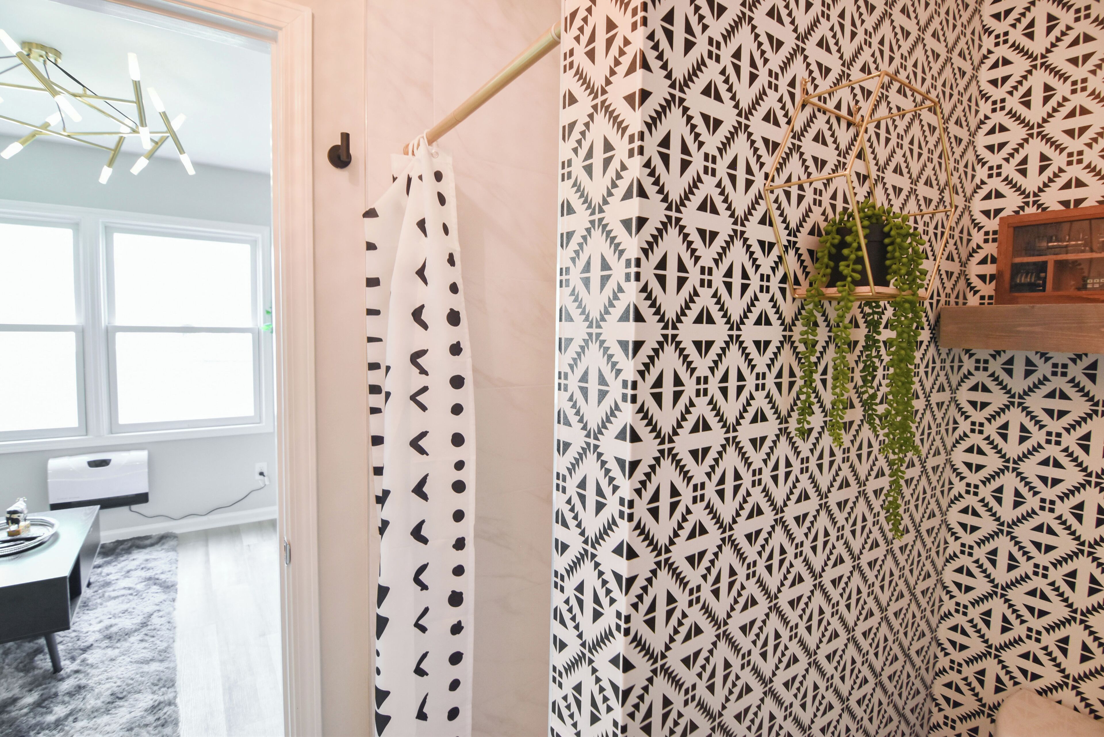 A bathroom with a geometric patterned shower curtain, a hanging plant, and a wooden shelf with toiletries.