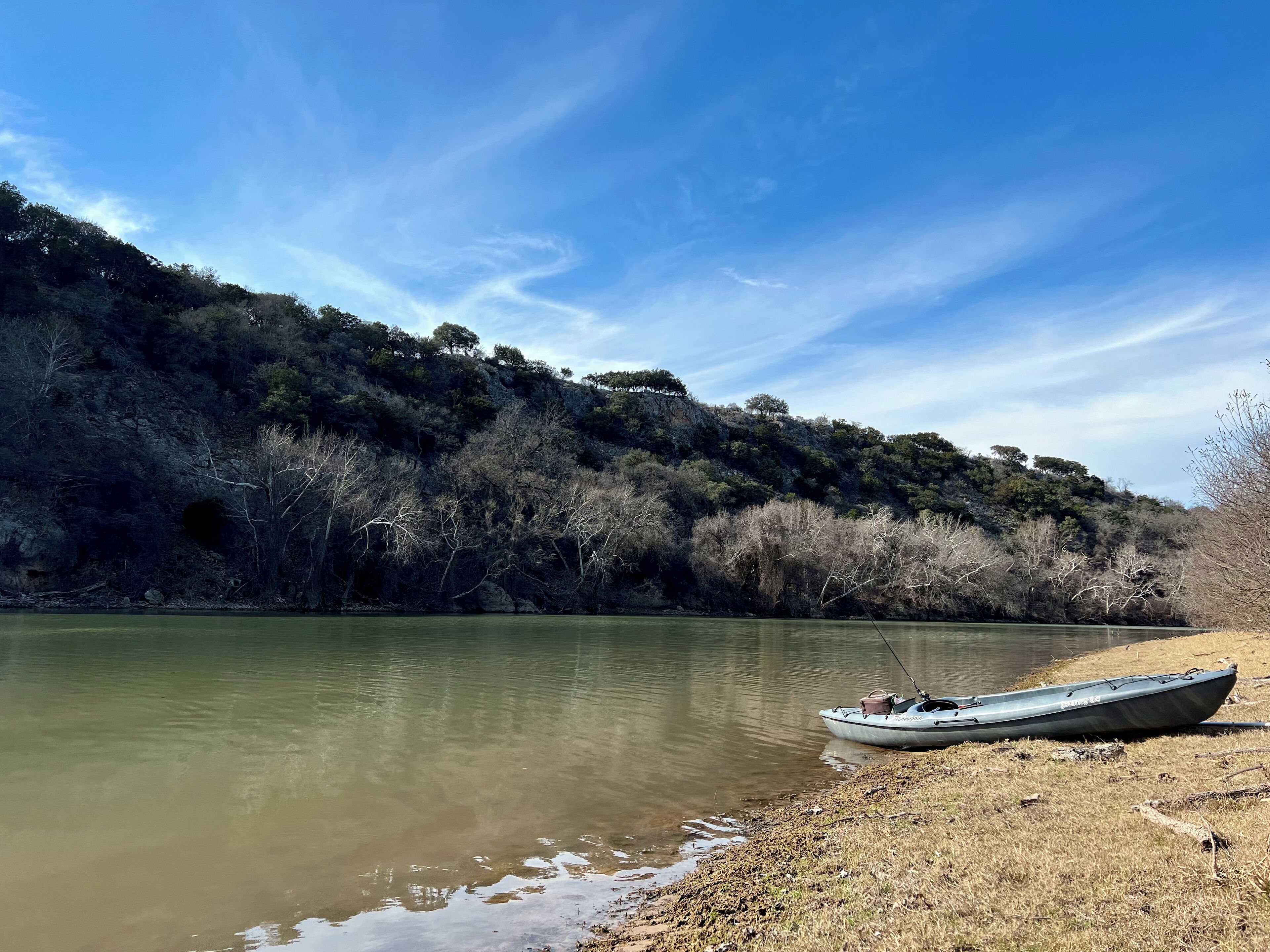 Una barca sulla riva di un fiume, con una collina boscosa sullo sfondo.