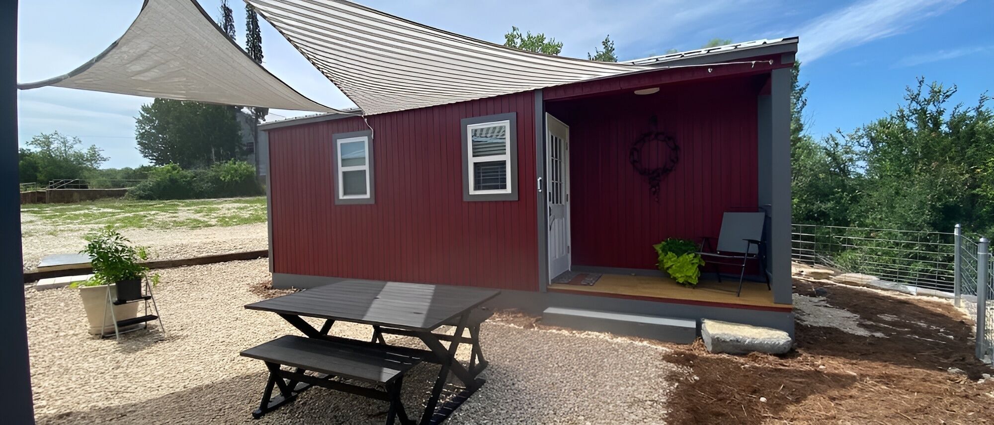 A red building with a covered patio, a table, and a chair.