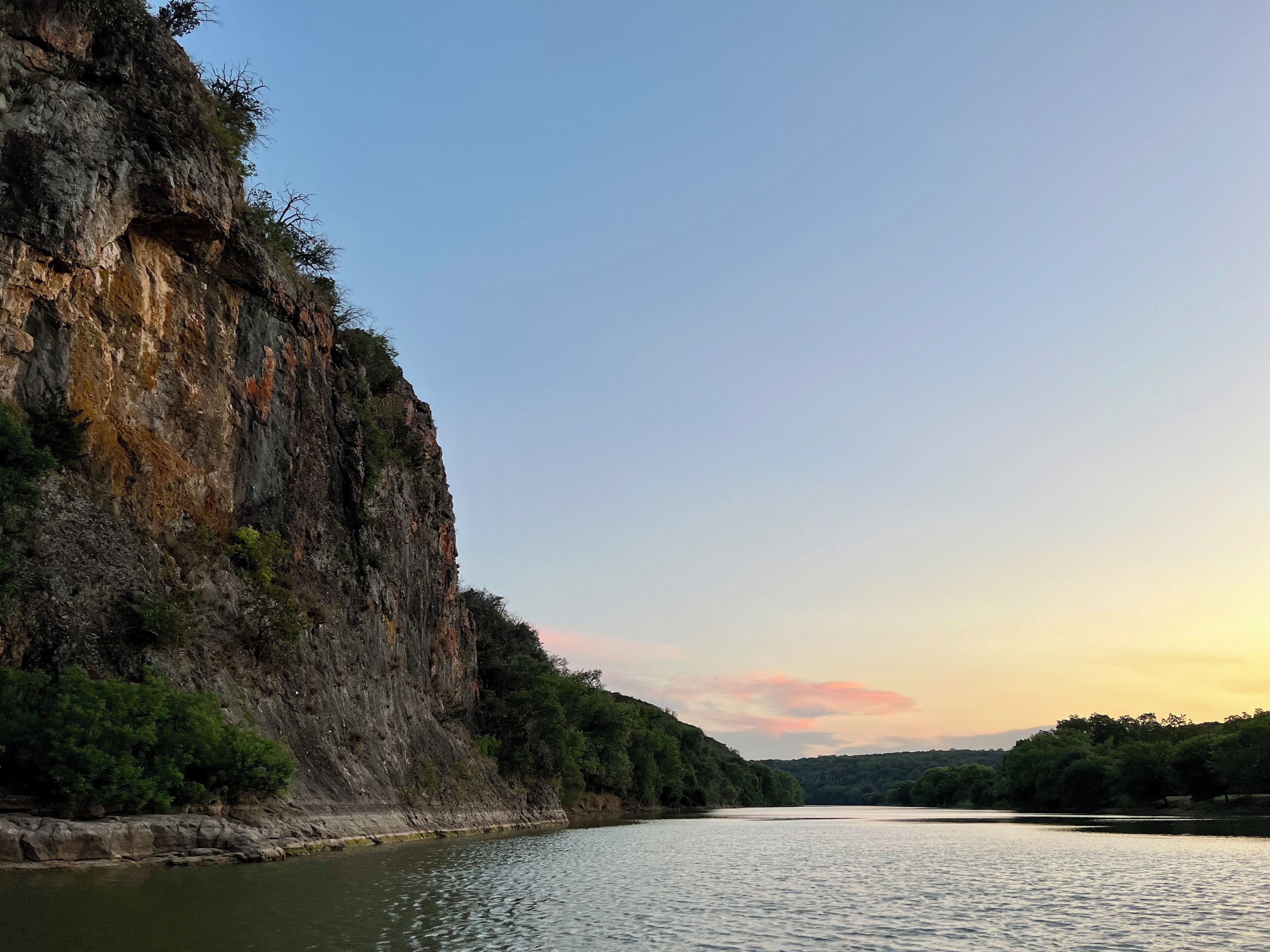 Une rivière bordée d’une falaise rocheuse d’un côté et d’une zone boisée de l’autre.