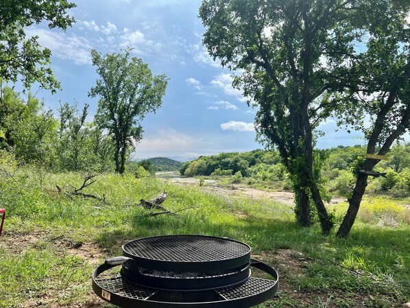 A grill in a natural setting with trees and a river in the background.