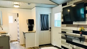 Una habitación de hotel moderna con una cama, un televisor montado en la pared, una cafetera y una pequeña cocina.