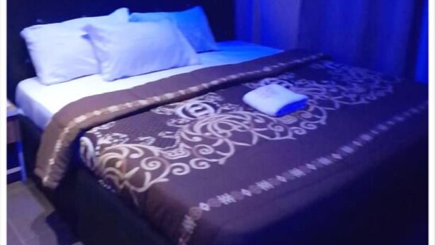 Un lit bien fait, avec une couvre-lit à motifs et des oreillers, une table de chevet et un mur éclairé d’une lumière bleue.