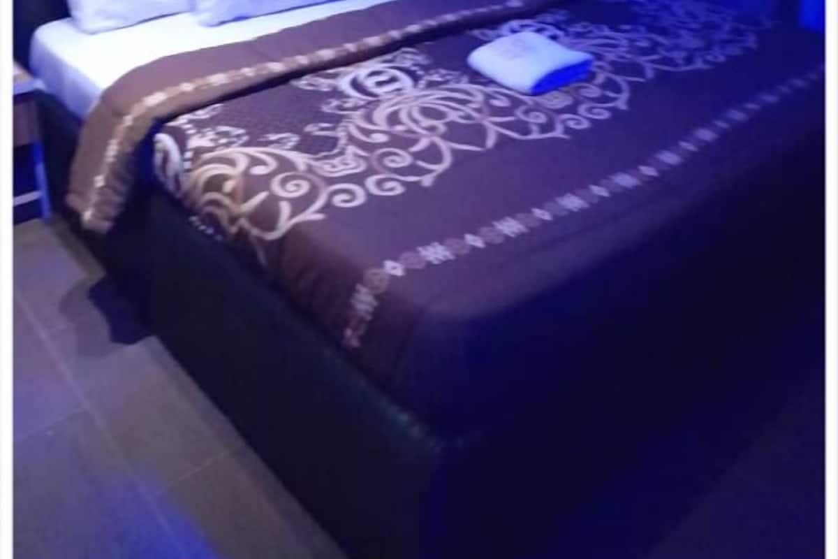 Een net opgemaakt bed met een beddegoed met een patroon en kussens, een nachtkastje en een blauw verlichte muur.