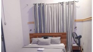 Une chambre à coucher avec un lit, une table de chevet, un ventilateur et un rideau.