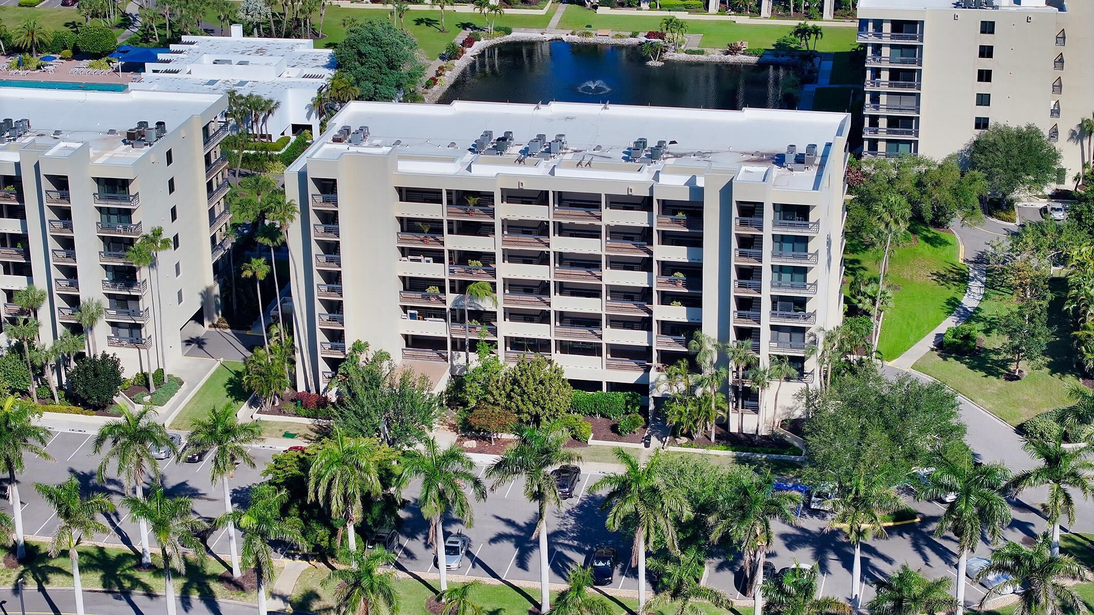 A high-rise building with multiple balconies, surrounded by palm trees and a parking lot.