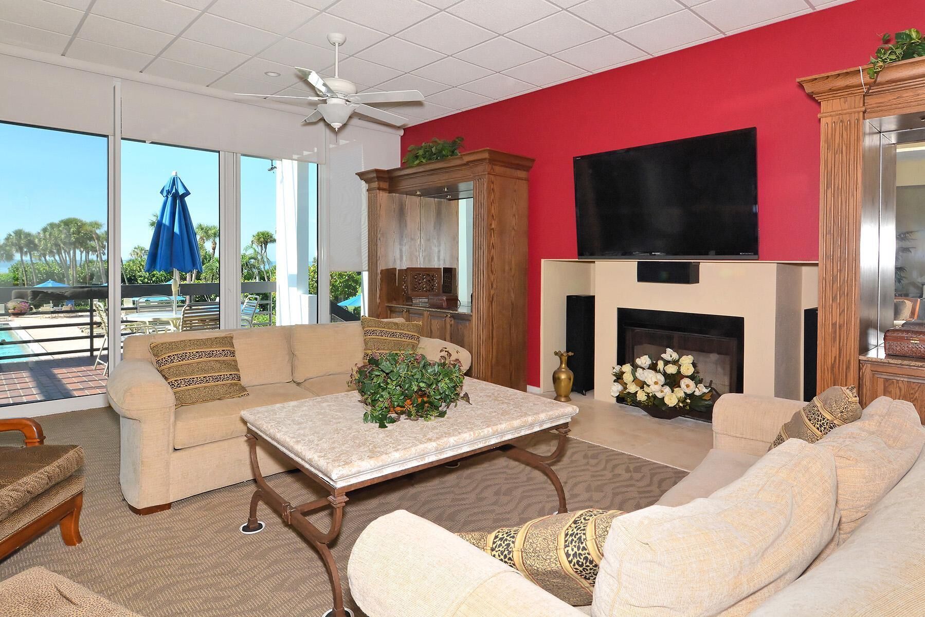 A spacious living room with a large window, a fireplace, and a pool view.