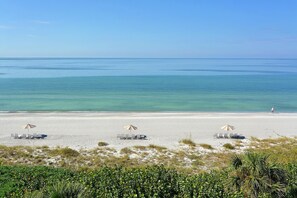 A beach with several sun umbrellas and lounge chairs arranged on the sand. - Partial Beach View 2 Bedroom Condo (Longboat Key)