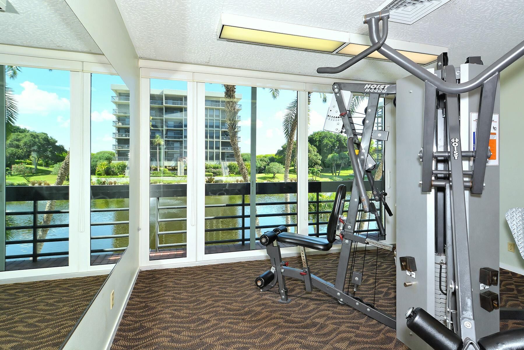 A gym with exercise equipment and large windows overlooking a water body and greenery.