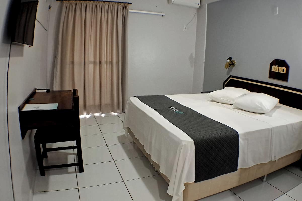 Habitación de hotel con cama, escritorio, silla, mesita de noche y televisor en la pared.