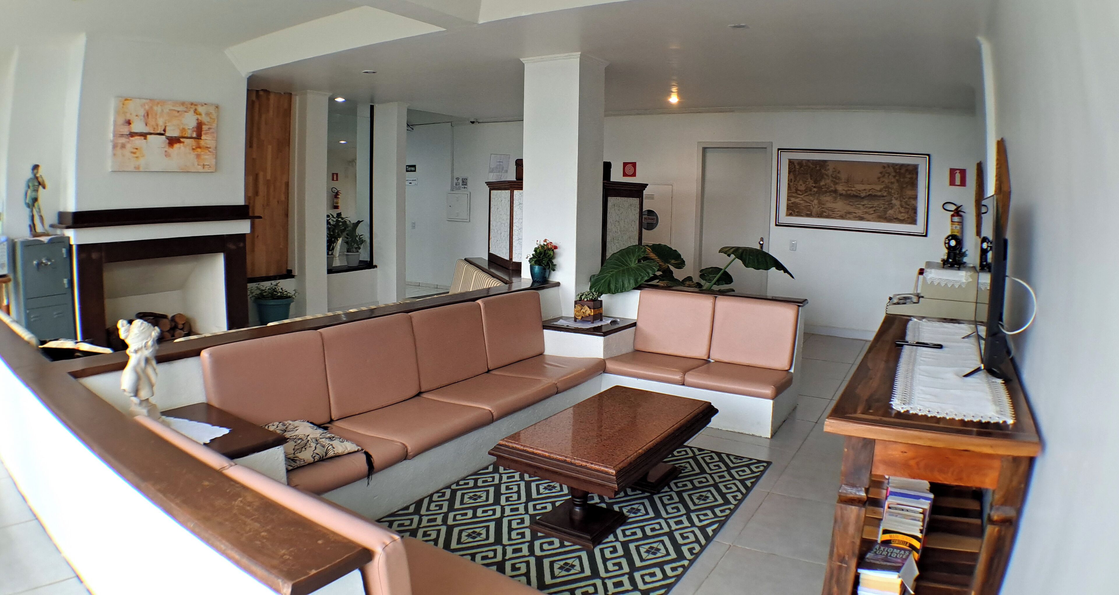A spacious living room with a large L-shaped sofa, a coffee table, and a bookshelf. There is a fireplace, a painting on the wall, and a potted plant.