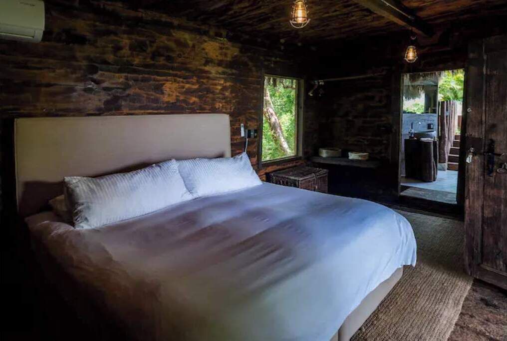 Quarto com uma cama grande, paredes de madeira e vista para o exterior.