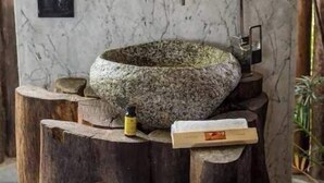 Un tabouret rustique en bois, surmonté d’un lavabo en pierre et doté d’un robinet moderne.