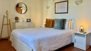 A neatly arranged bedroom with a bed, bedside tables, a nightstand, a mirror, and a framed certificate on the wall. - Grupo Morgado (Tavira)