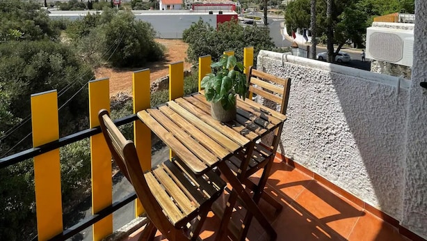 A balcony with a wooden table and chairs, overlooking a coastal area with buildings and palm trees. - Grupo Morgado (Tavira)