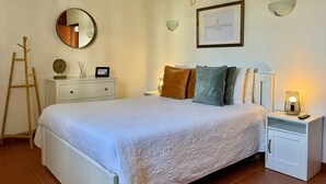 Une chambre à coucher bien rangée, avec un lit, des tables de chevet, une commode, un miroir et un certificat encadré accroché au mur.