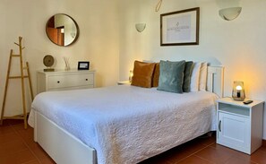 Un dormitorio ordenado con cama, mesitas de noche, un espejo y un certificado enmarcado en la pared.