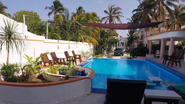 A swimming pool with lounge chairs and a covered area, surrounded by palm trees and a white building. - El Paraiso de Capitán Fernando Apartamento 4 (Chelem)