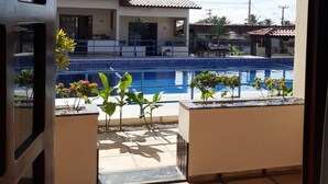 A view from a balcony with a pool, palm trees, and a building with a tiled roof. - Hotel Pousada Canoa Quebrada (Aracati)