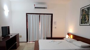 A hotel room with a bed, a TV, a desk, and a window with curtains. - Hotel Pousada Canoa Quebrada (Aracati)