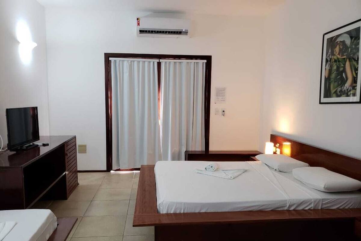 A hotel room with a bed, a TV, a desk, and a window with curtains.