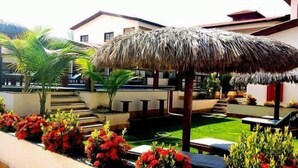 A patio area with a thatched umbrella, outdoor seating, and potted plants. - Hotel Pousada Canoa Quebrada (Aracati)
