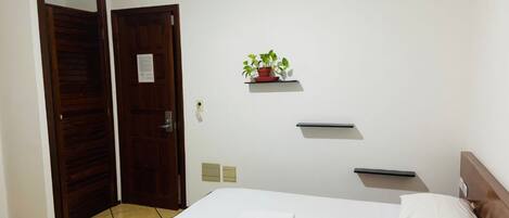 Habitación de hotel con cama, puerta de madera, un pequeño estante con una planta y suelo de baldosas.
