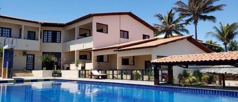 A hotel with a swimming pool, multiple balconies, and palm trees.