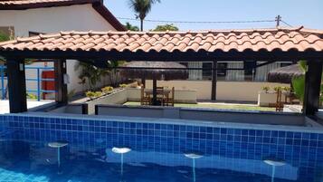 A swimming pool with blue tiles, a covered seating area, and a thatched roof structure.