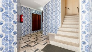 A hallway with patterned blue and white tiles, a fire extinguisher, a wooden door, and a staircase with beige steps. - VIVA  Nanda's  Place (Porto)
