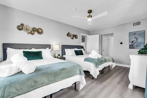 Een hotelkamer met twee bedden, een plafondventilator, een schilderij van een vogel en een witte dressoir.