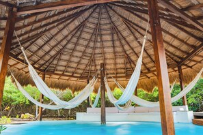 A hammock under a thatched roof structure with a pool in the foreground. - U-GO Magnífica casa con piscina junto al Mar (Cartagena)