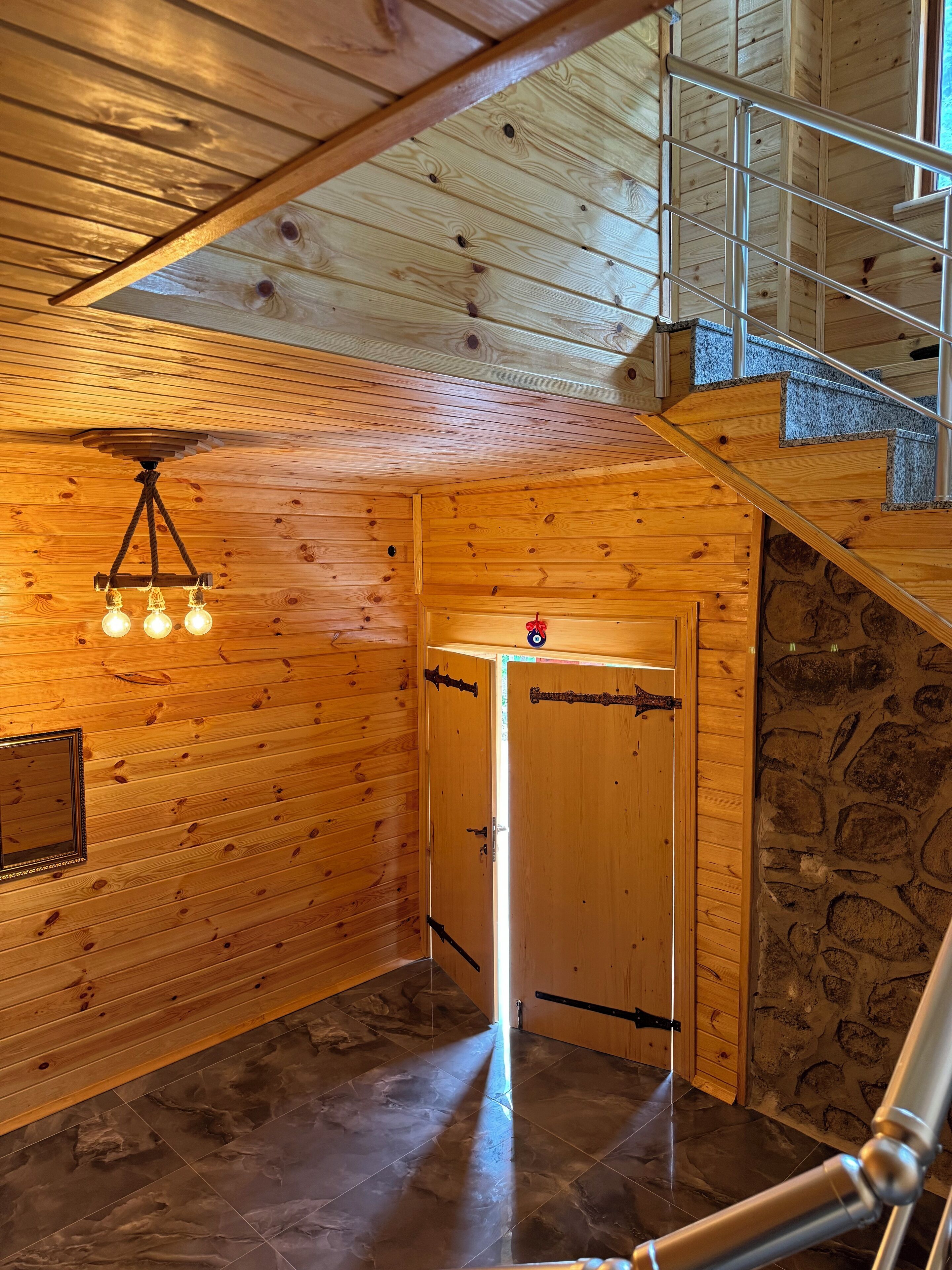 A wooden interior with a staircase, a ceiling light fixture, and a stone wall.