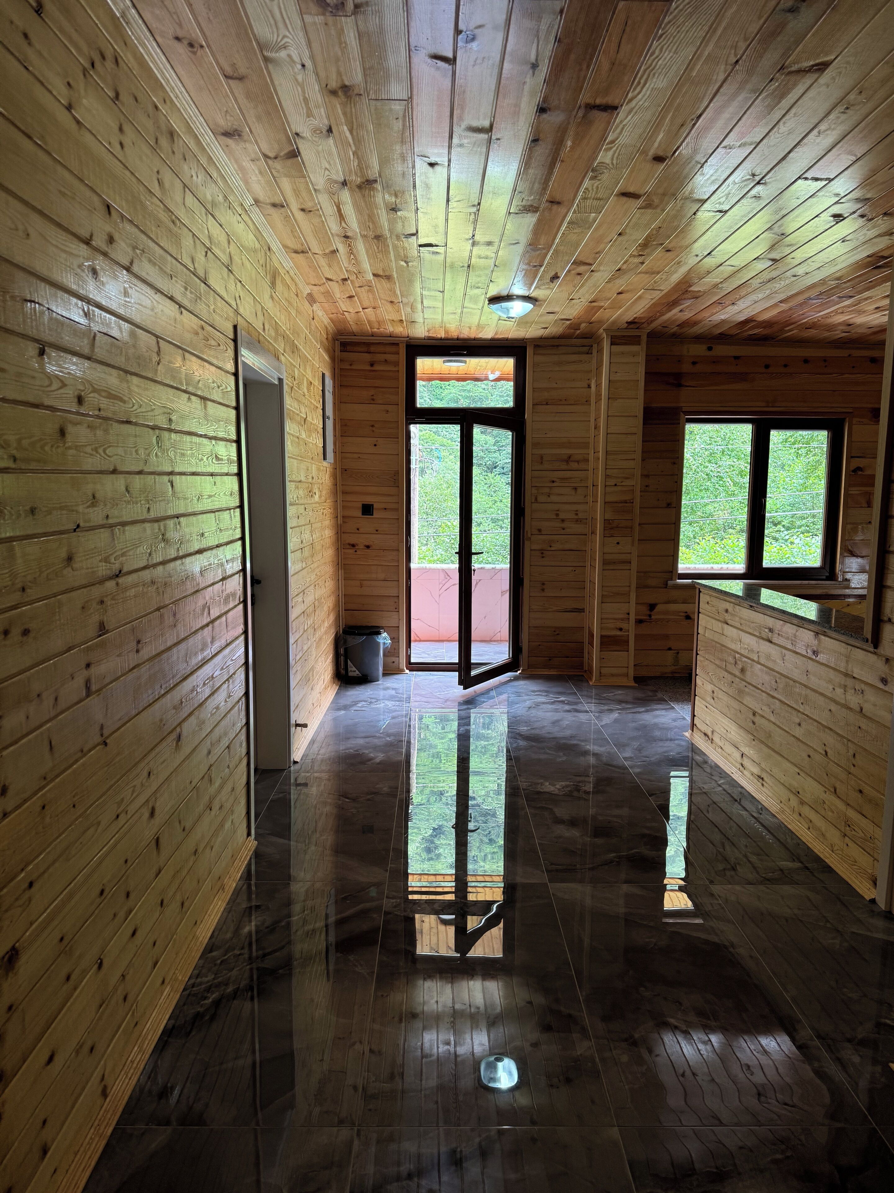 Un interior de madera con piso pulido, una puerta que da al exterior y una ventana con vistas a follaje.
