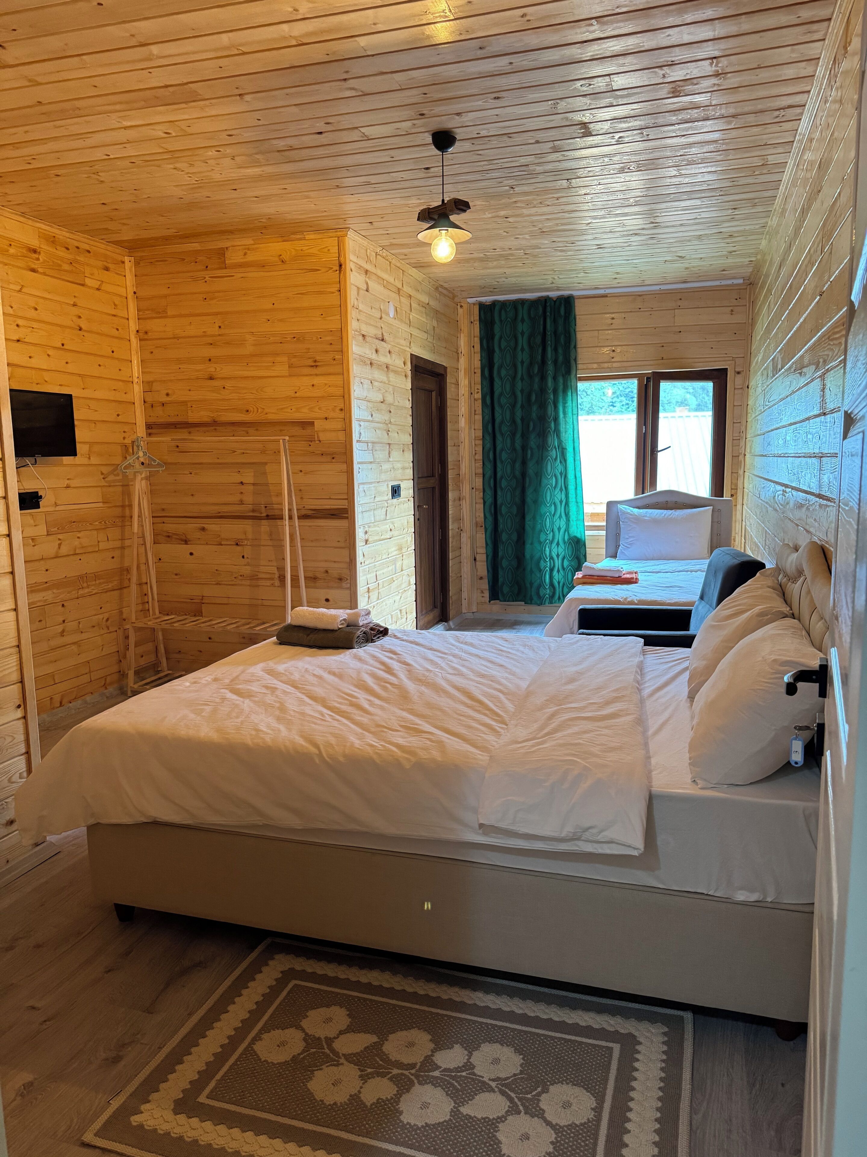 Quarto de cabana de madeira com cama, uma mesinha e um candeeiro suspenso.