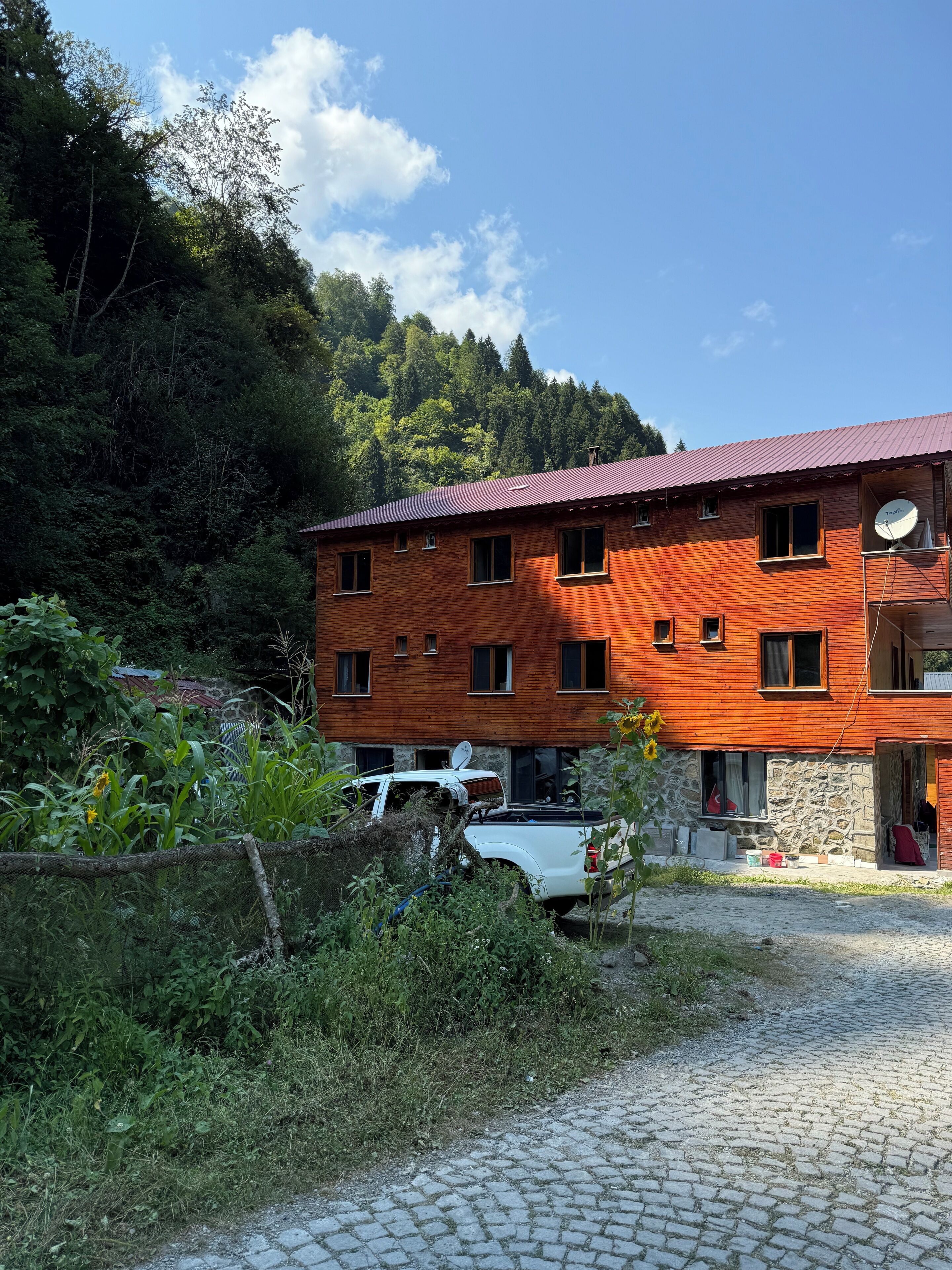 A two-story wooden building with a red roof, a satellite dish, and a stone foundation.