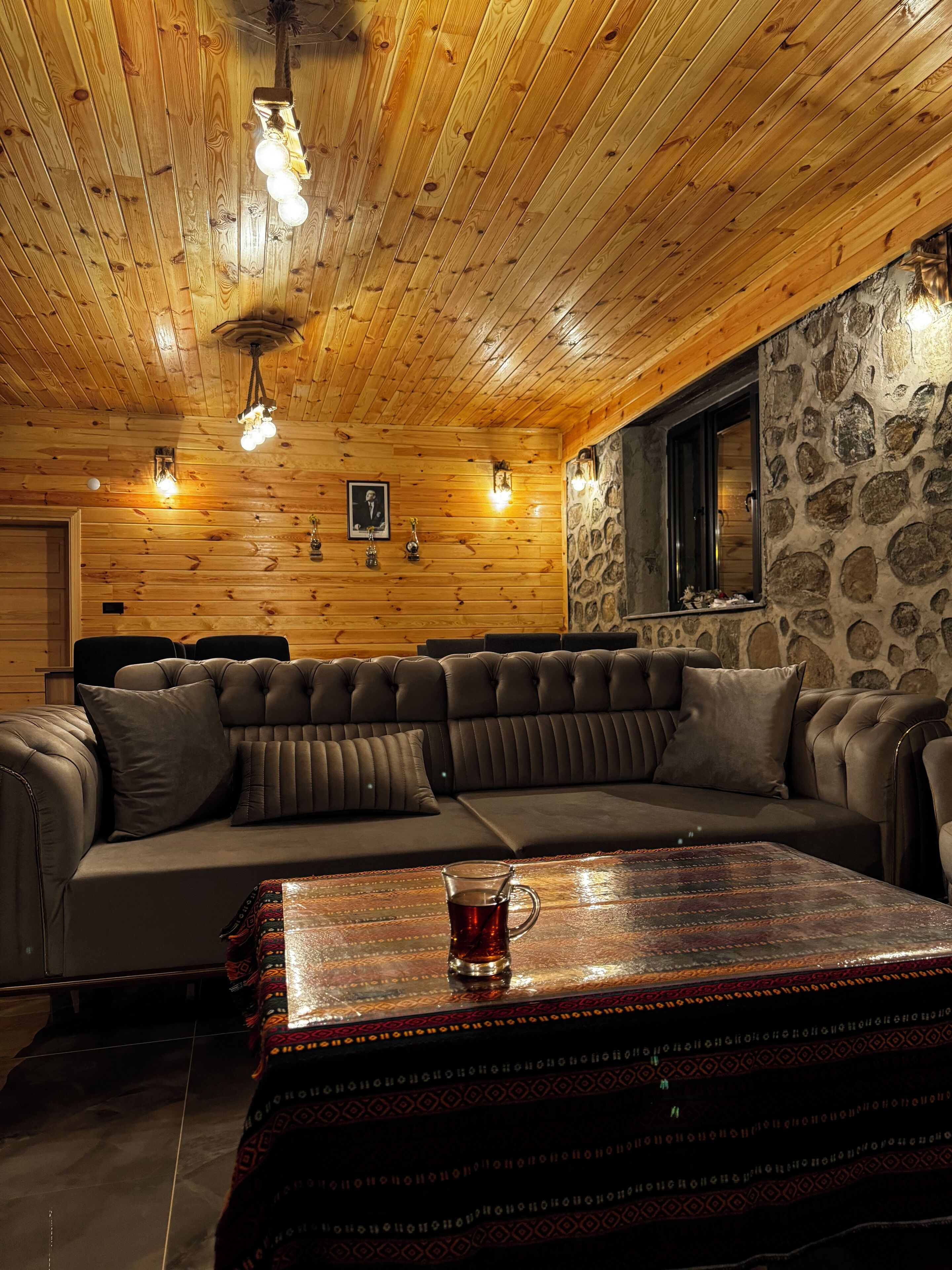 A cozy log cabin interior with a sectional sofa, a wooden ceiling, stone walls, and a rustic ambiance.