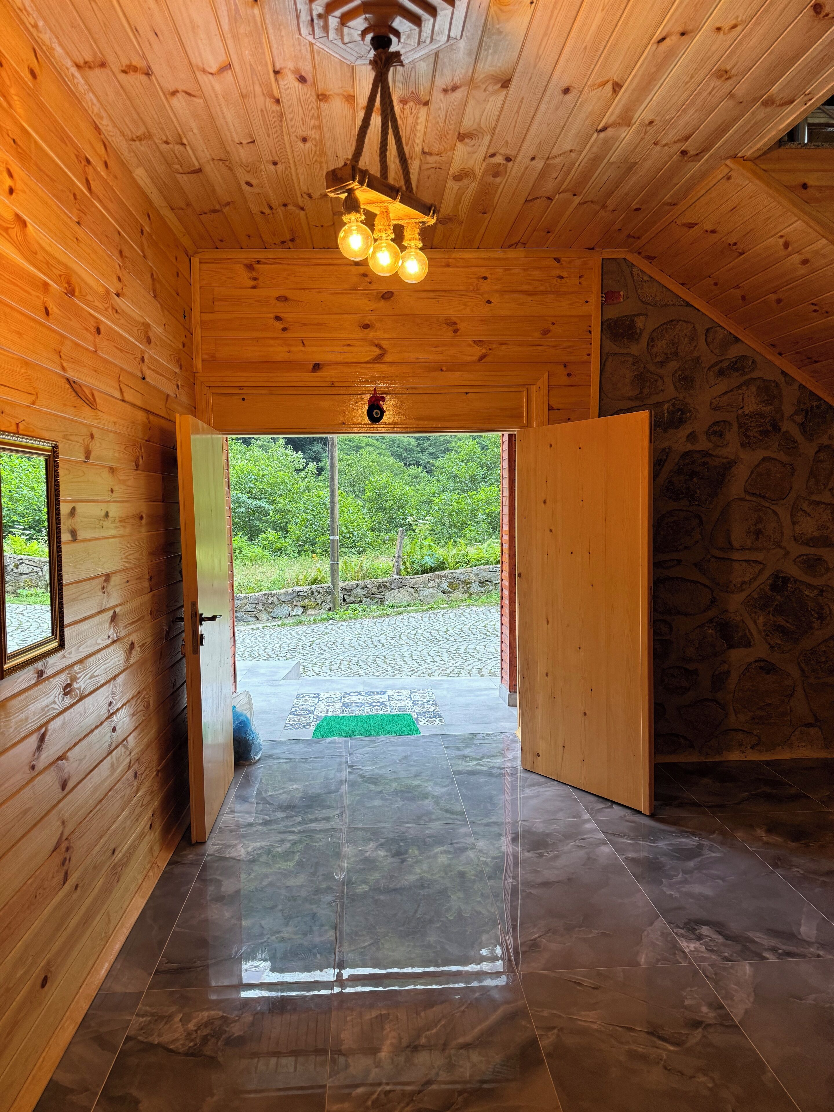 A wooden interior hallway with a tiled floor, a wooden door, and a view of greenery outside.