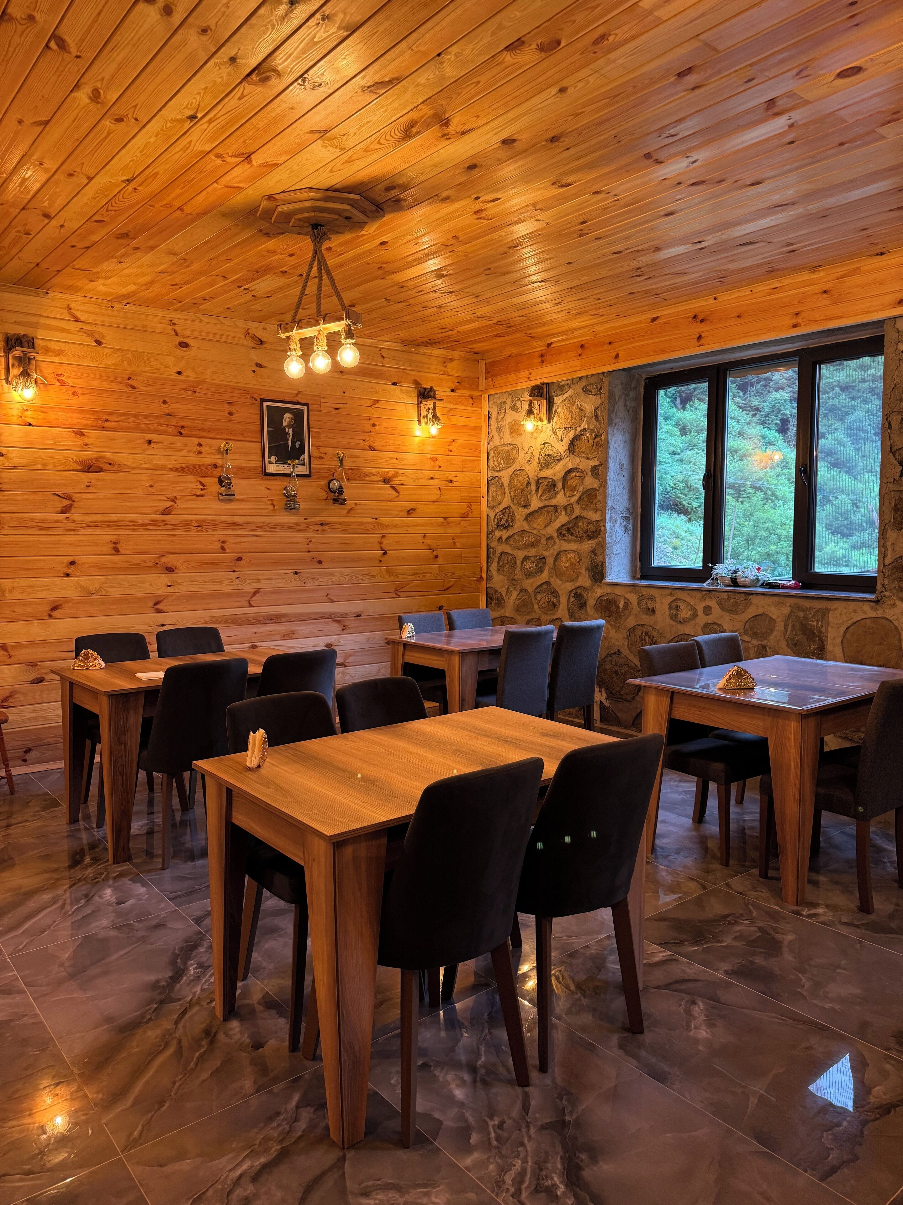 Un interior de madera con mesas y sillas, una pared de piedra y una ventana con vistas.