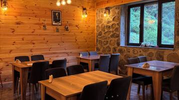 Un interior de madera con mesas y sillas, una pared de piedra y una ventana con vistas.