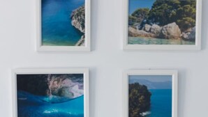 A white table with a decorative glass object on it, set against a wall with four framed coastal landscape paintings. - Central Seaview Apartment by PikHost (Vlorë)