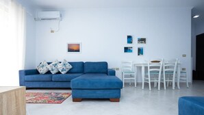 A modern living room with a blue sofa, a dining table with chairs, and a small rug. - Central Seaview Apartment by PikHost (Vlorë)