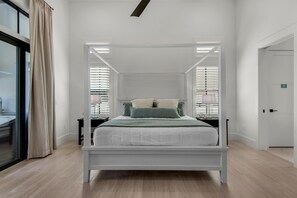 A modern bedroom with a four-poster bed, white walls, and a large window with blinds. - Casa Mar (Destin)