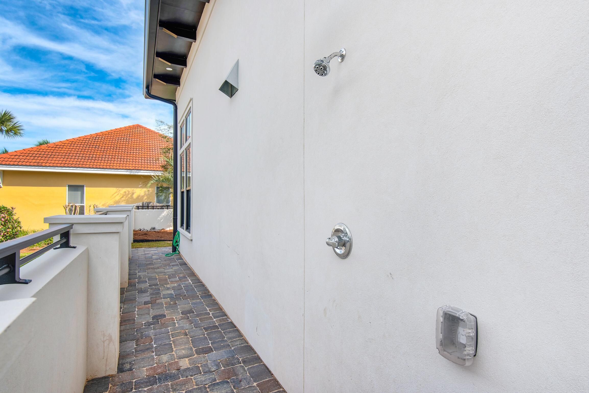 Un estrecho pasillo exterior con suelo de baldosas, pared blanca y barandilla de metal.